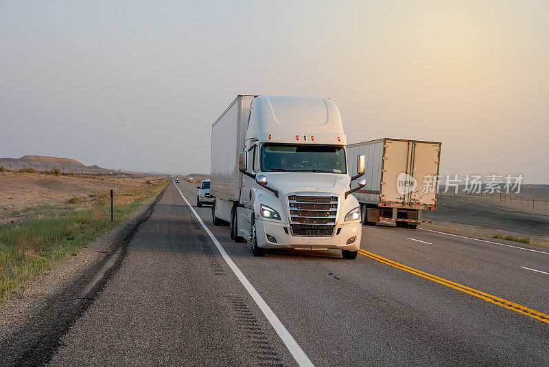 黄昏时分，在戏剧化的天空下，半卡车在犹他州沙漠的高速公路上超速行驶