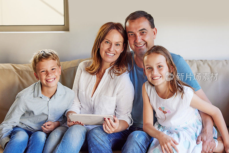 一个幸福的家庭坐在家里的沙发上，一起使用数字平板电脑