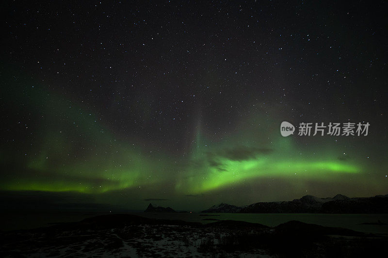 北极光在夜空中山脉的轮廓。长曝光，多色灯光