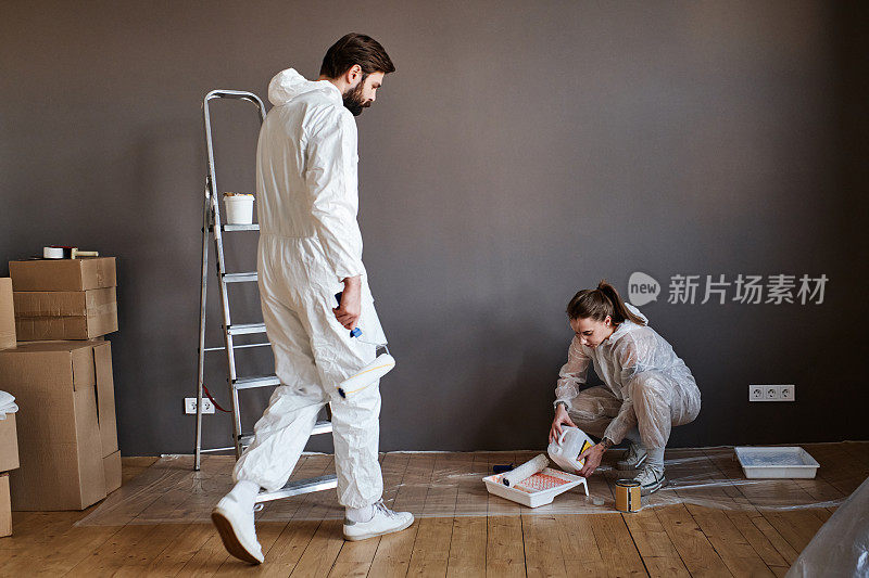 现代的年轻男女穿着防护服在他们的公寓里修理墙壁