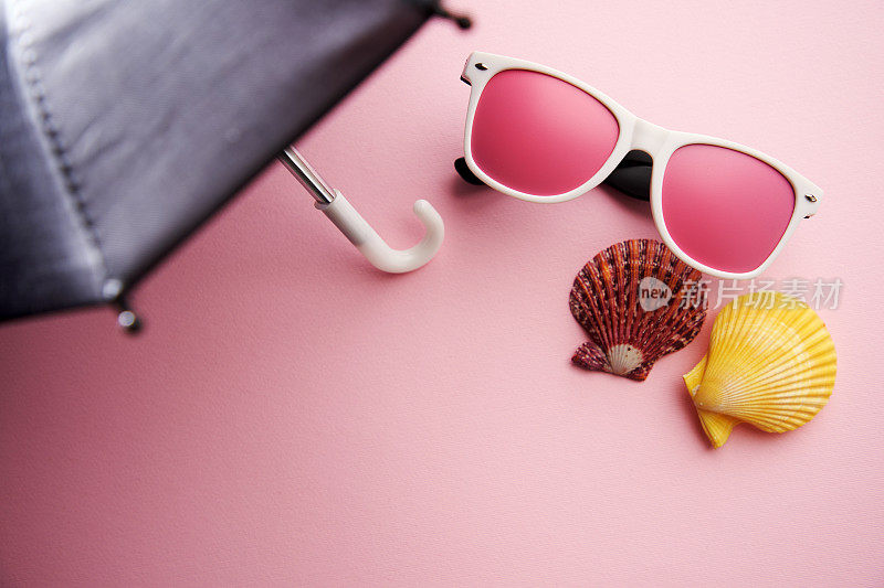 粉红色太阳镜和贝壳在伞的阴影下
