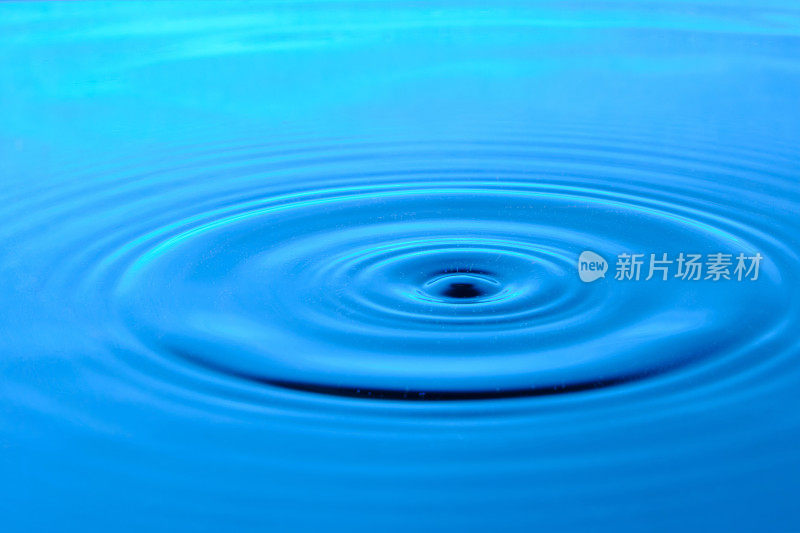 明亮的蓝色背景与发散的圆圈从水滴表面的水。