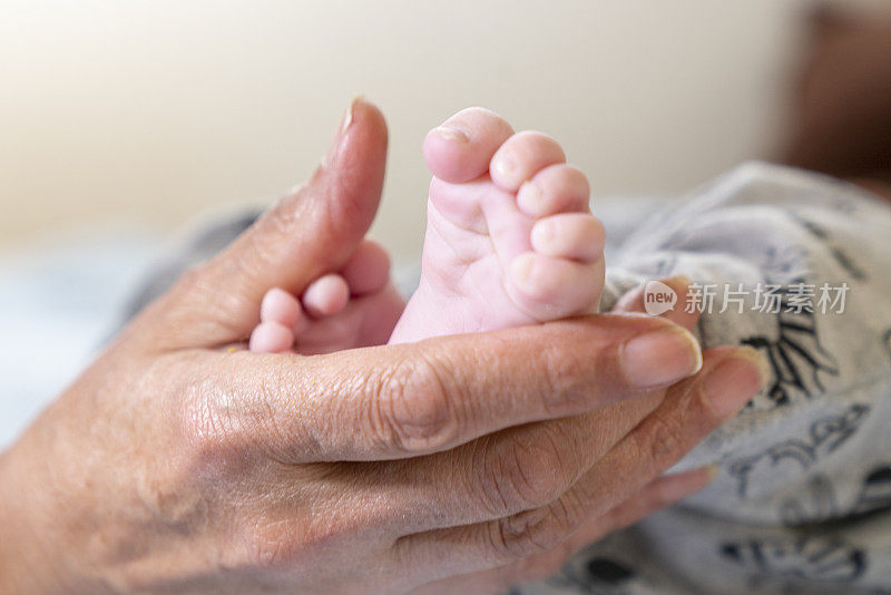 奶奶抱着孩子的脚。母亲的手和孩子的脚。家庭的概念