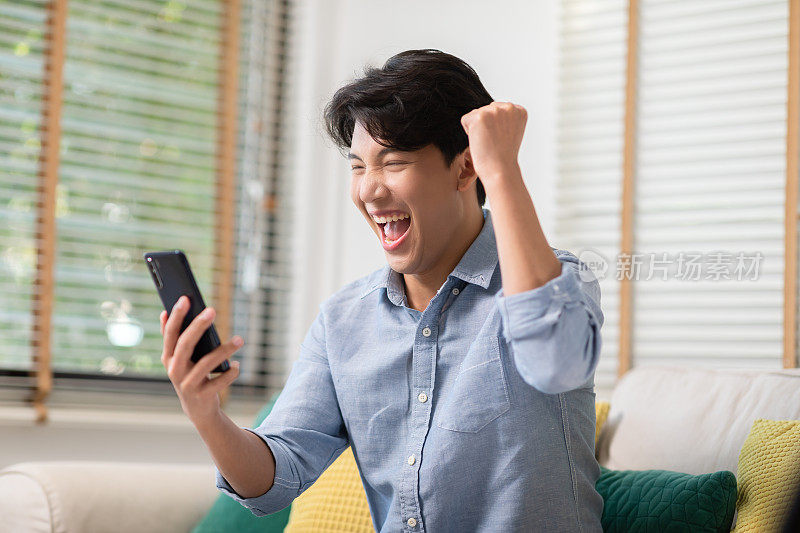 一名亚洲男子在手机屏幕上微笑着，表达着自己的快乐。他得到了好消息，面露喜色。科技可以帮助我们有更方便的联系。