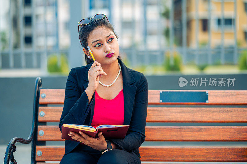 年轻的大学生坐在公园的长椅上思考新的想法，并把它们写在日记上。