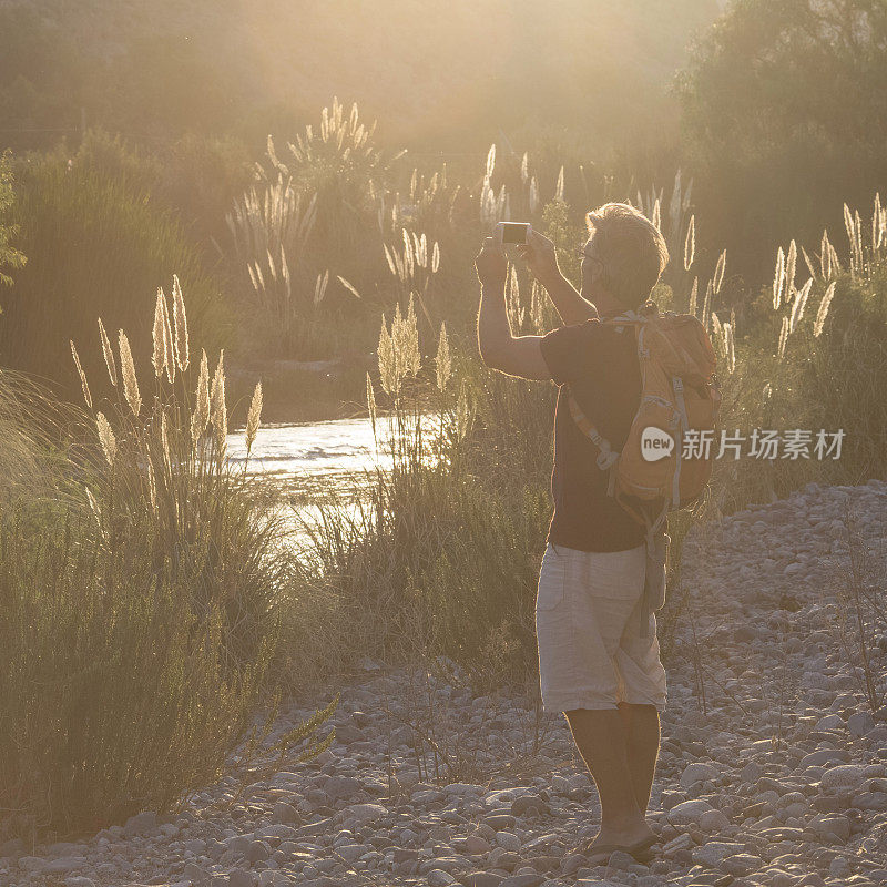 徒步旅行者在河流和草原上拍摄日落