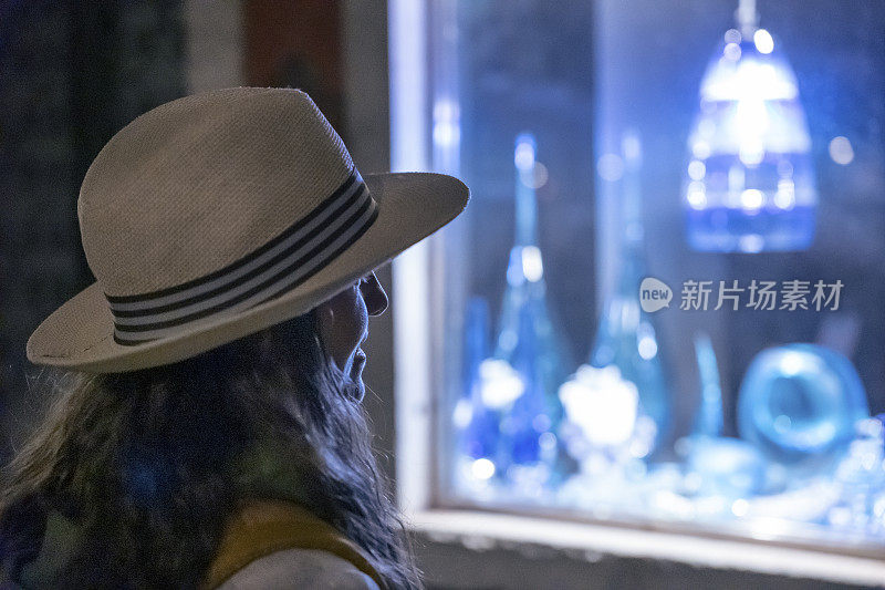 在Murano岛度假的女人看着玻璃艺术的商店橱窗。