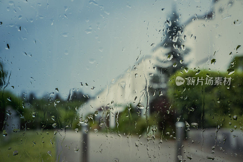 雨滴落在窗户上，背景是郊区的街道。