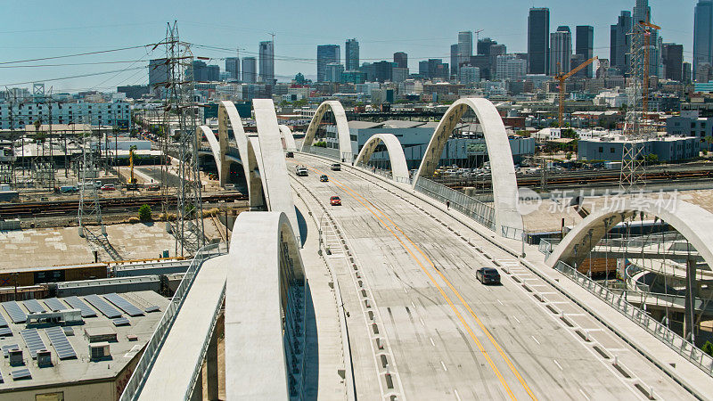 从空中拍摄的汽车驶过第六街大桥，远处是加利福尼亚州的洛杉矶市中心