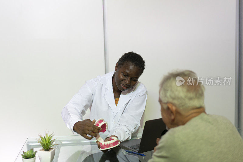 非裔美国女牙医向老年病人展示使用塑料下颚的正确口腔卫生