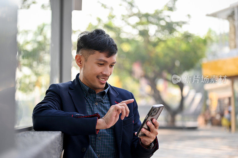 快乐的亚洲商人在城市等公交车或出租车时使用智能手机。
