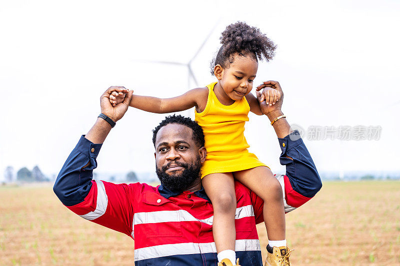 非洲黑人工程师父亲抱着他的女儿在他的怀里，在风力涡轮机非常自由。环境工程，可再生能源，热爱自然，热爱家庭的理念