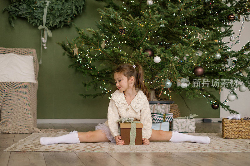 一个体操女孩手里拿着礼物，在圣诞树下摆着麻绳的姿势