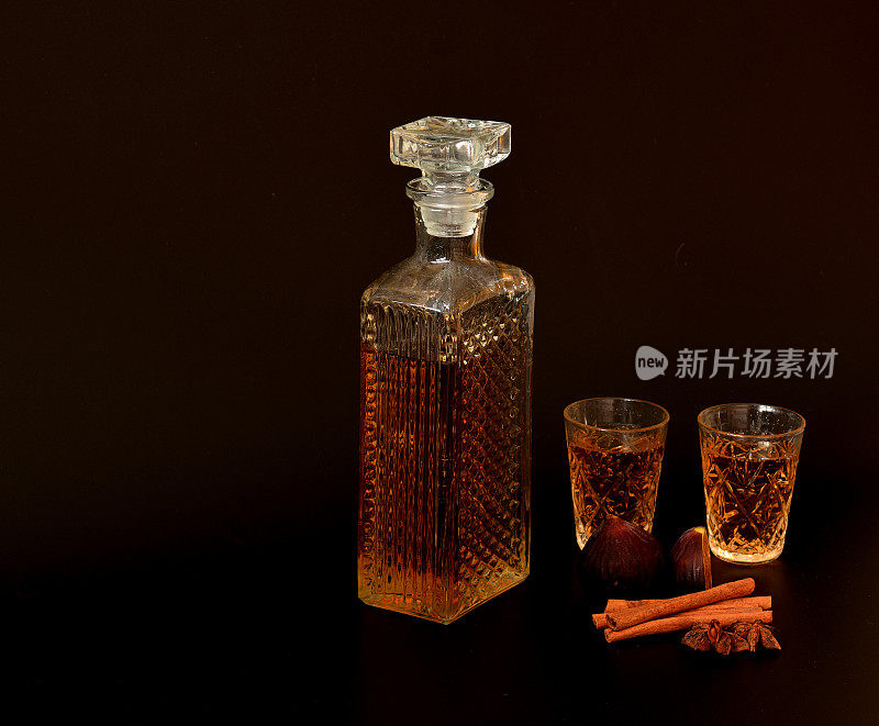 无花果利口酒与肉桂和茴香在黑色的背景，一个水晶醒酒器和两个玻璃杯与香料和成熟的水果旁边浓烈的酒精。