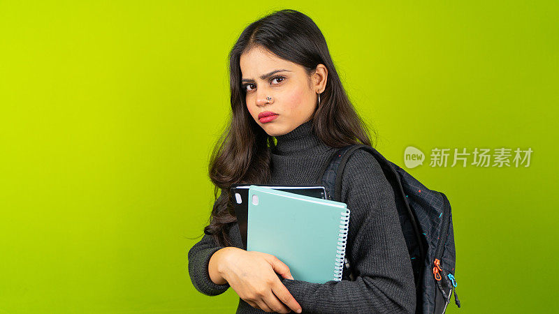 年轻的印度女学生背着背包，拿着书，不开心，悲伤，或压力大的大学女孩孤立在绿屏色度键背景