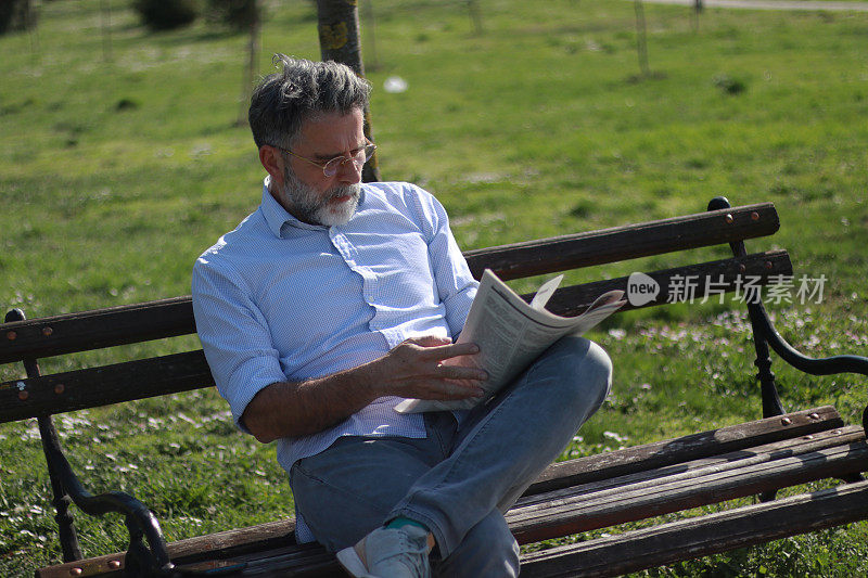 成熟的男人在公园里看报纸