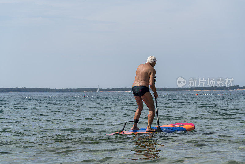 年长的男子站着在海浪上划桨