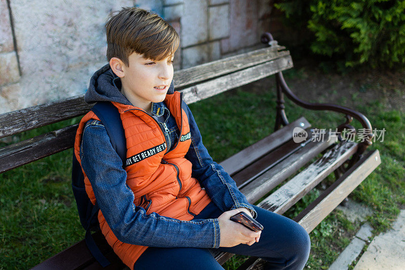 男生放学后要回家。他正坐在公园的长椅上。他正在和朋友进行视频通话。