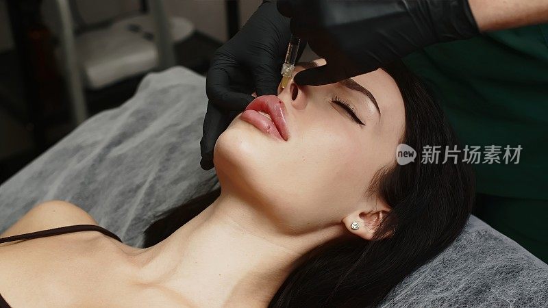 一名外科医生戴着医用手套，小心翼翼地用注射器将透明质酸注入一名妇女的嘴唇。丰唇手术。注射美容。