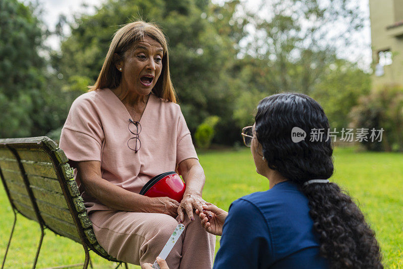 拉丁裔妇女在养老院里负责照顾她，她在花园里享受户外活动，由她的照顾者陪同