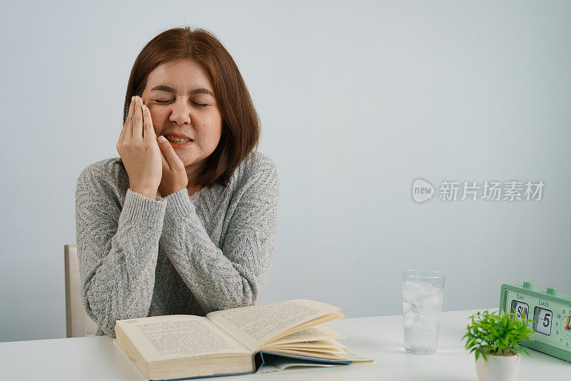 年轻的亚洲女子喝加冰的水，摸自己的脸颊，忍受牙痛，对寒冷有情绪反应。