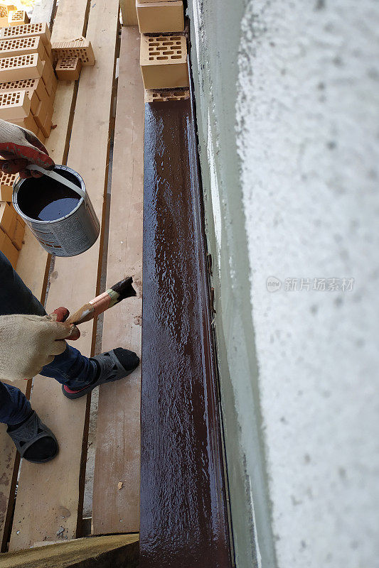 一名在建筑工地工作的男子用棕色油漆把金属角涂上。