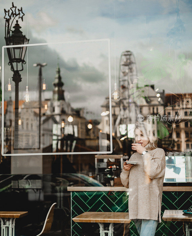 一名女子坐在咖啡馆里，置身于绿色和白色的装饰之中，一边品尝咖啡，一边全神贯注地玩手机。充满活力的氛围为现代生活方式概念提供了生动的背景