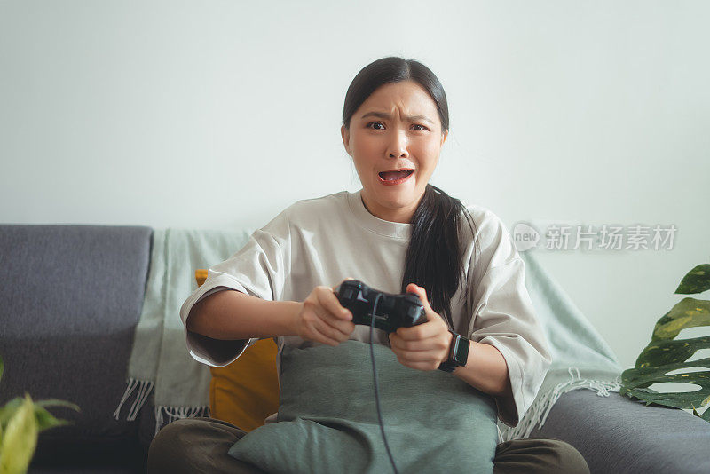 亚洲女子在输了游戏后坐在家里的沙发上，用操纵杆玩游戏，感觉很沮丧。