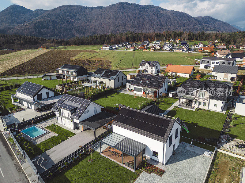 低空近景新密集农村住宅开发，大多是灰色屋顶，一些绿色景观，小树。有平屋顶的现代住宅