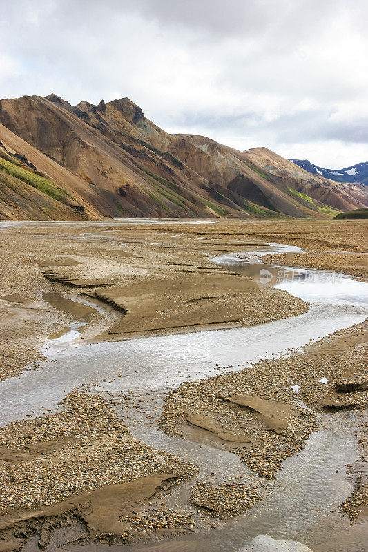 冰岛Laugevegur步道起点的Landmannalaugar周围引人注目的山景，显示了洪水平原上的冰川径流河