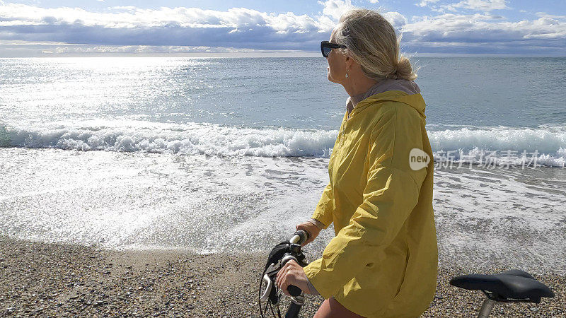 成熟的女人推着自行车沿着空旷的海滩
