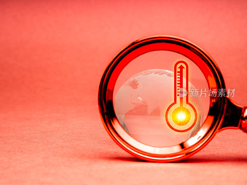 全球变暖和温室效应的概念。高温天气温度计高温图标符号和玻璃地球仪在放大镜镜头的特写，红色背景与复制空间。