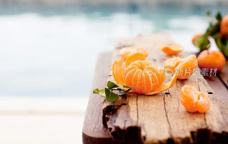 新鲜的橘子放在一张蓝色的木桌上，以大海、水景为背景