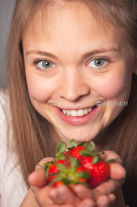 漂亮的女孩拿着草莓与牙齿微笑
