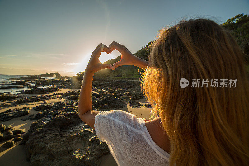 年轻女子把海滩上的夕阳画成心形