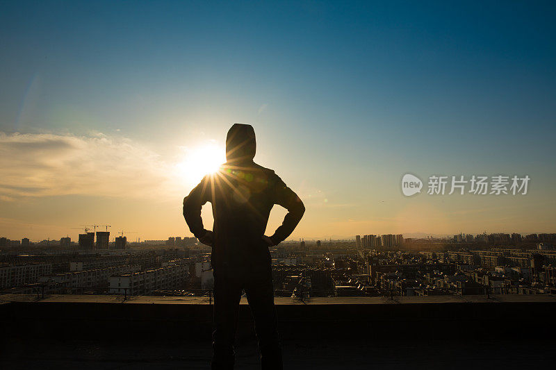 年轻人站在屋顶上，看着城市的夕阳