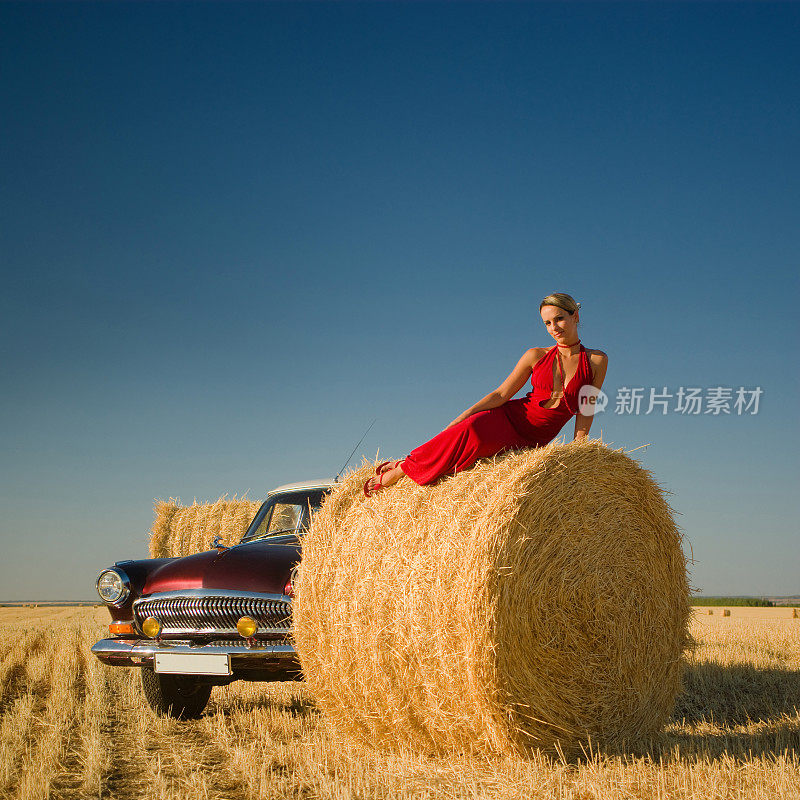 女孩躺在稻草捆上，背景是复古的汽车