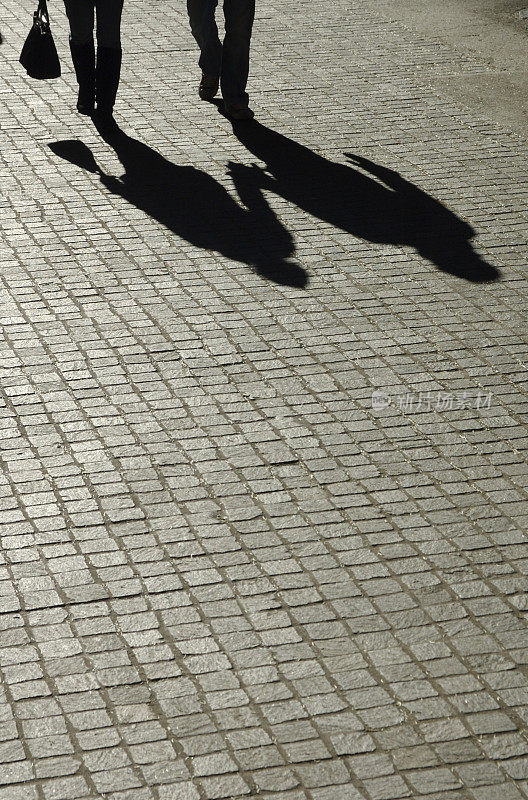 影子夫妇手牵着手走在鹅卵石街上