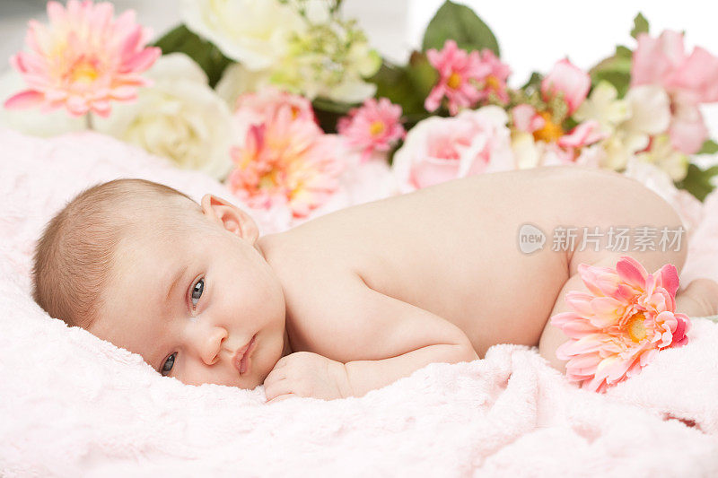 刚出生的婴儿在带花的粉红色毯子上醒来