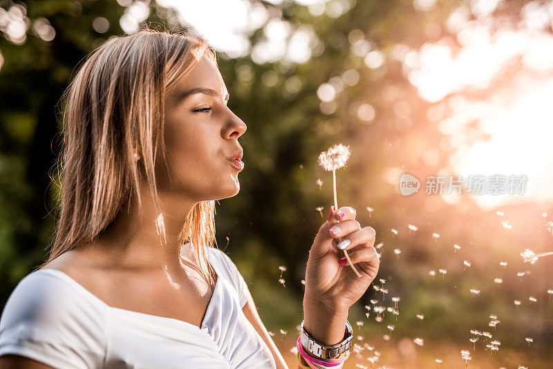 年轻美丽的女人在夕阳下吹蒲公英。