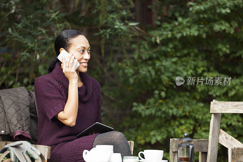 正在玩手机的女人坐在花园里喝着咖啡