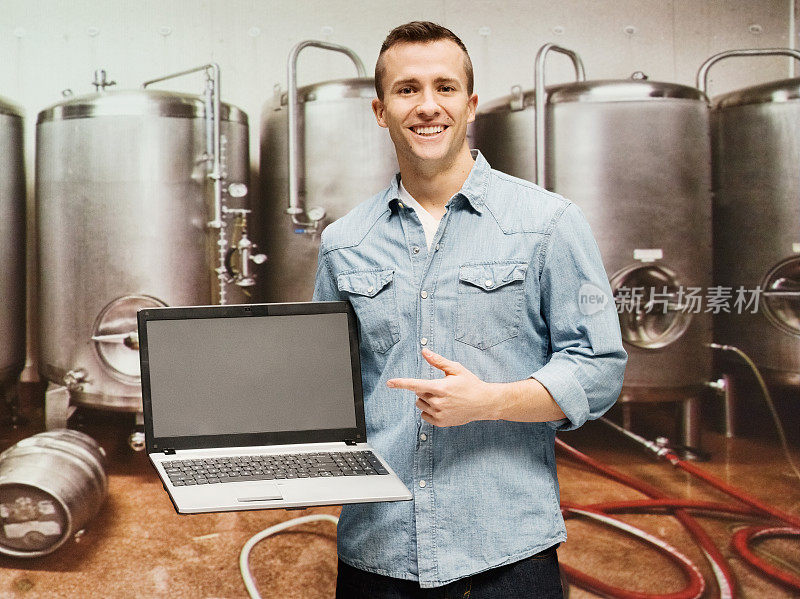 一个微笑的男人指着啤酒厂的笔记本电脑