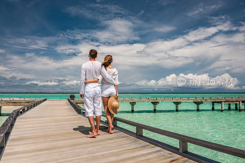 一对穿着白色衣服的夫妇在马尔代夫的海滩码头上