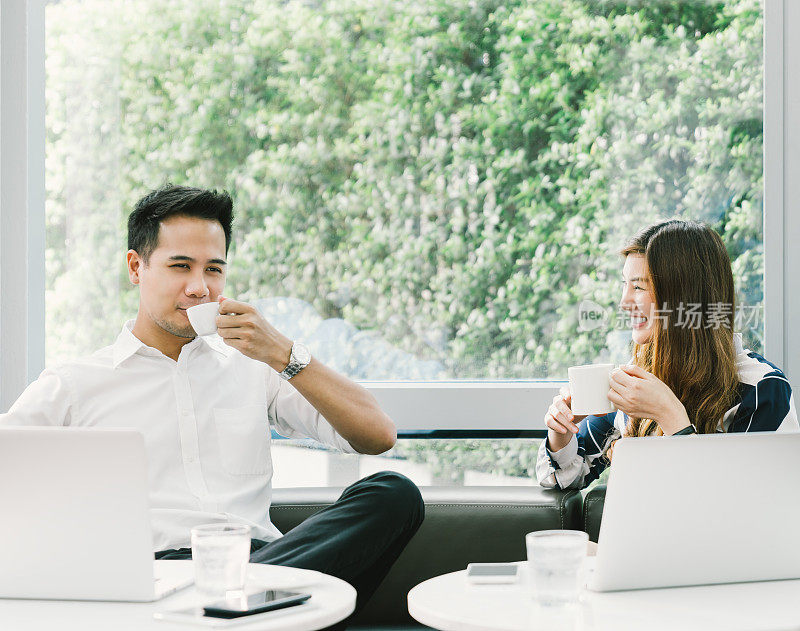 年轻的亚洲夫妇或同事在咖啡馆或咖啡店用笔记本电脑工作的时候喝咖啡休息。休闲、工作、爱情、友情概念。与复制空间