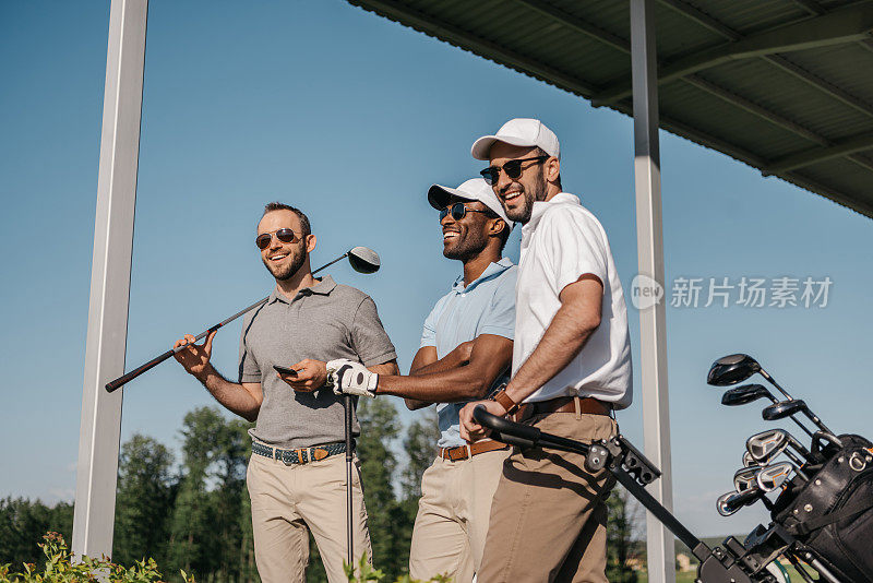 三个戴着太阳镜的男人在户外拿着高尔夫球杆，面带微笑