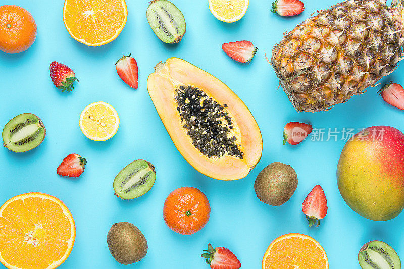 不同热带季节夏季水果品种。木瓜，芒果，橘子，柑橘，橙子，菠萝，柠檬，草莓，猕猴桃在蓝色的背景。健康生活方式饮食维生素。平躺