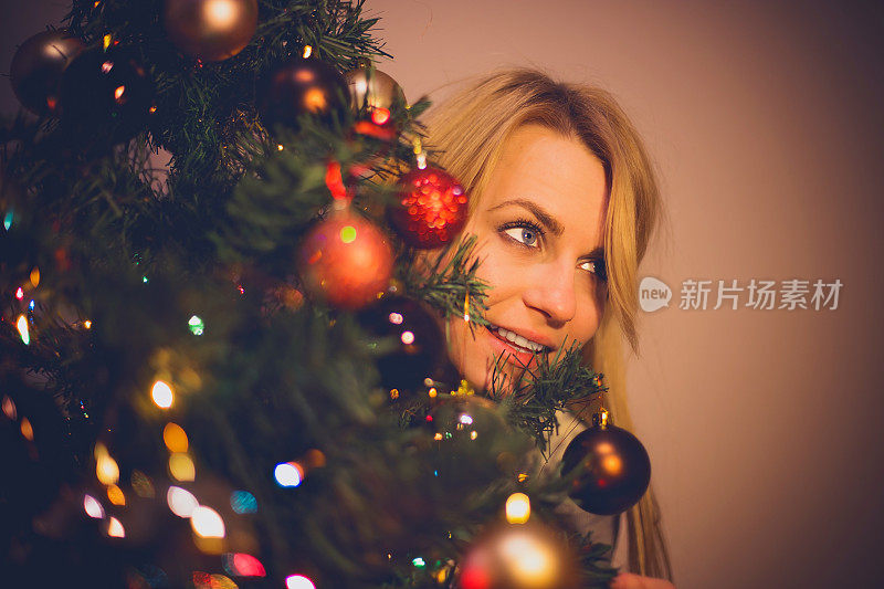 年轻的金发女人躲在圣诞树后面