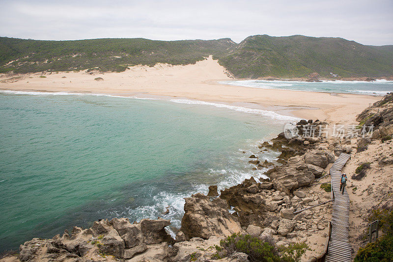 一个喜欢冒险的人沿着海岸在木板路上徒步旅行