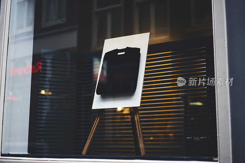 时尚的展位架上有一件黑色的基本折叠t恤，上面有你的logo或品牌名称的模拟复制空间，和衣服一起展示在商店的橱窗前面