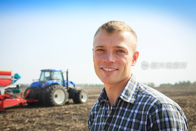 年轻有魅力的男人在拖拉机旁边。农业的概念。